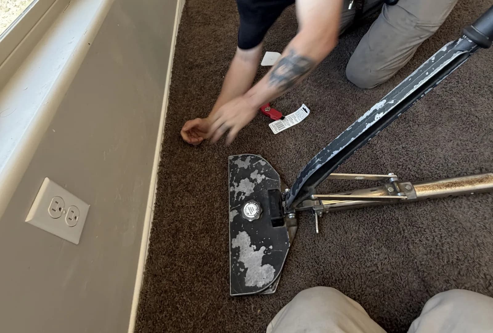 Aggie technician hooking carpet onto the tack strip beside a power stretcher during a carpet re-stretch