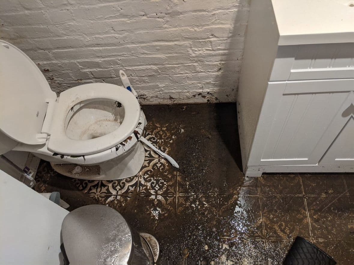 Sewage backup spread across a bathroom tile floor around the base of a toilet in a Las Cruces home